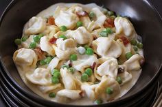 a black bowl filled with pasta and peas on top of a table next to silverware