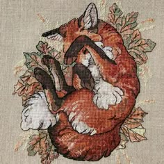 the cross stitch pattern shows an orange fox with leaves on it's back and its tail curled up