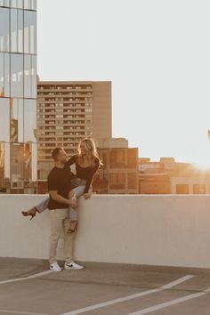 a man holding a woman on top of a roof next to tall buildings in the background