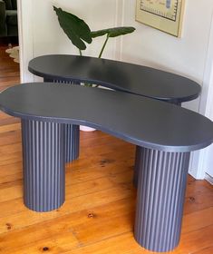 two black tables sitting on top of a hard wood floor next to a potted plant