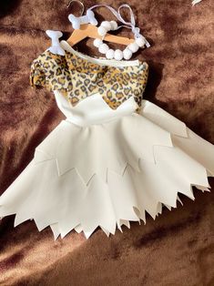 a dress made out of paper and some hair clips on top of a brown blanket