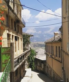 an alley way with buildings and flowers on the side, in front of a mountain range