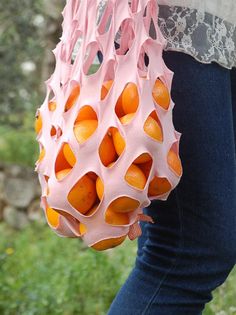 a woman holding a pink bag with oranges in it's center and holes on the inside