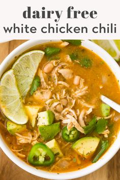 a white bowl filled with chicken chili soup and topped with avocado, limes and sliced jalapenos