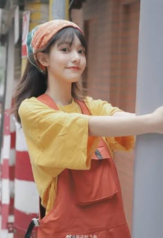 a woman in an orange apron is leaning against a pole