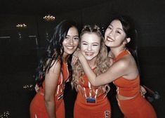 three girls in orange outfits are posing for the camera with their arms around each other