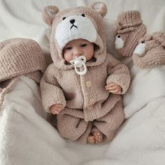 a baby in a bear suit laying on top of a bed with two teddy bears