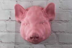 a pink pig mask hanging on a brick wall next to a white brick wall with the face of a pig