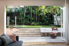 a living room filled with furniture next to a lush green yard covered in palm trees