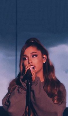 a woman standing in front of a microphone with her hands on her face and mouth