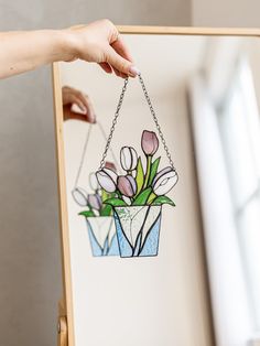 a hand holding a piece of stained glass with flowers hanging from it's side