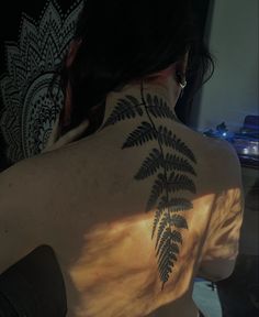 the back of a woman's shoulder with a fern tattoo on her left side