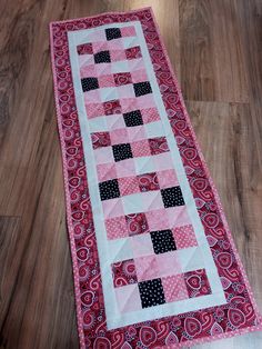 a pink and black quilted table runner on the floor with wood floors in the background