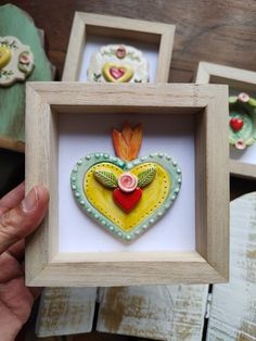 three framed pictures with flowers and leaves in them, one is holding a heart shaped brooch