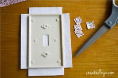 a white light switch plate sitting on top of a wooden table next to a pair of scissors