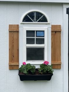 a window with wooden shutters and two flower boxes in front of it on the side of a white building