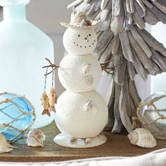 a snowman made out of seashells sitting next to a bottle and glass ornament