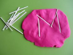 a pink piece of paper with sticks sticking out of it on a green surface next to some straws