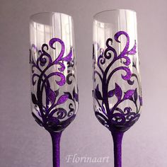 two wine glasses decorated with purple flowers and vines on them, sitting side by side