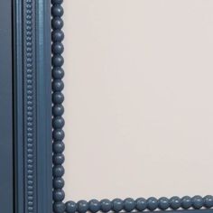 an ornate blue frame with beaded trim around the edges is shown in front of a plain white wall