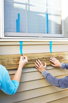 two people attach tape to the side of a house's exterior window sill