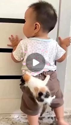 a baby standing next to a cat on top of a floor