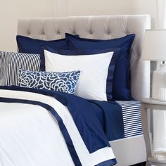 a bed with blue and white pillows on top of it next to a night stand