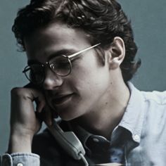 a young man wearing glasses talking on a cell phone while holding his hand to his ear