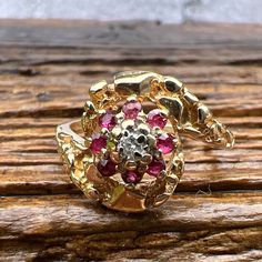 Gorgeous Synthetic Rubies accented by a Diamond set in a unique 14k Yellow Gold Nugget Flower Ring. US Size 5 1/2 Widest Point measures approximately 12.3 mm. Back of the shank tapers down to 1.3 mm, approximately. Nicely weighted at 3 grams, approximately. Stamped 14K Ruby is the birthstone for July. Diamond is the birthstone for April. Flower Shaped 14k Gold Jewelry, Collectible Yellow Gold Jewelry With Center Stone, 14k Gold Flower Jewelry With Prong Setting, Unique Gemstone Cluster Ring In Yellow Gold, Formal 14k Gold Flower Jewelry, Heirloom 14k Gold Flower Jewelry, Unique 14k Yellow Gold Ruby Ring, Gold Cluster Ring With Gemstone, Gold Cluster Ring With Birthstone