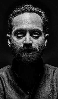 a black and white photo of a man with a beard wearing a leather jacket looking at the camera