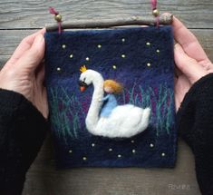 someone is holding up a small felt art piece that looks like a swan with a crown on its head