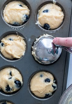 blueberry muffins in a muffin tin with a hand holding a spoon