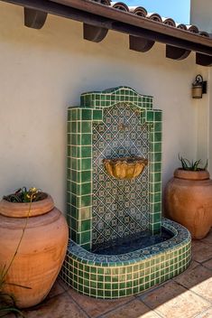 an outdoor fountain with potted plants and two large clay planters on the ground