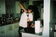 a man is using a hair dryer on his hair in the kitchen while another person stands behind him