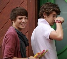 two young men standing next to each other in front of a green wall and wooden door