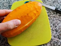 a person is holding an orange object on a cutting board