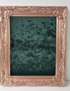 an ornate gold frame with green velvet in the center on a white wall behind it