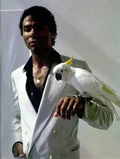 a man in a suit holding a white bird on his arm and looking at the camera