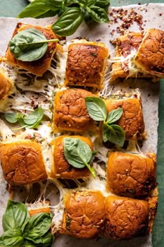 small sandwiches with cheese and spinach on a piece of parchment paper next to basil leaves