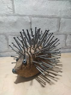 a hedgehog sculpture made out of nails on a wooden table next to a brick wall