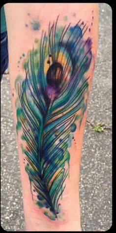 watercolor tattoo on the leg of a woman with a colorful peacock feather in it