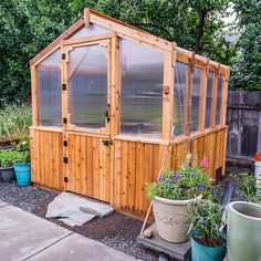 a small wooden building with lots of windows and plants in the front yard, next to a garden shed