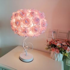 a pink lamp sitting on top of a white table next to a vase with flowers