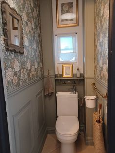 a toilet in a bathroom with floral wallpaper and framed pictures on the walls above it