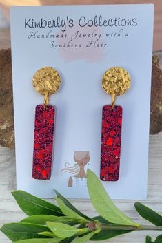 the red and gold earrings are sitting on top of a card next to some leaves