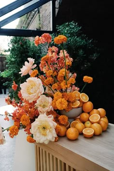 an arrangement of flowers and oranges on a table in front of some trees outside