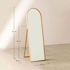 a tall wooden mirror sitting on top of a floor next to a white wall with measurements