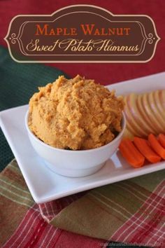 a white plate topped with carrots next to a bowl of hummus and crackers