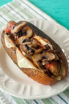 a sandwich with mushrooms and cheese is on a white plate next to a green tablecloth