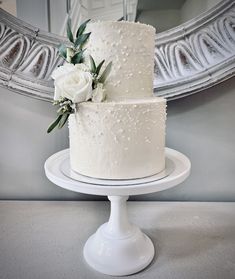 a white wedding cake sitting on top of a table in front of a round mirror